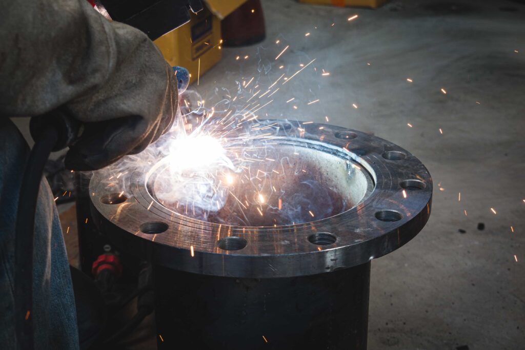 A man welding stainless steel flanges together.